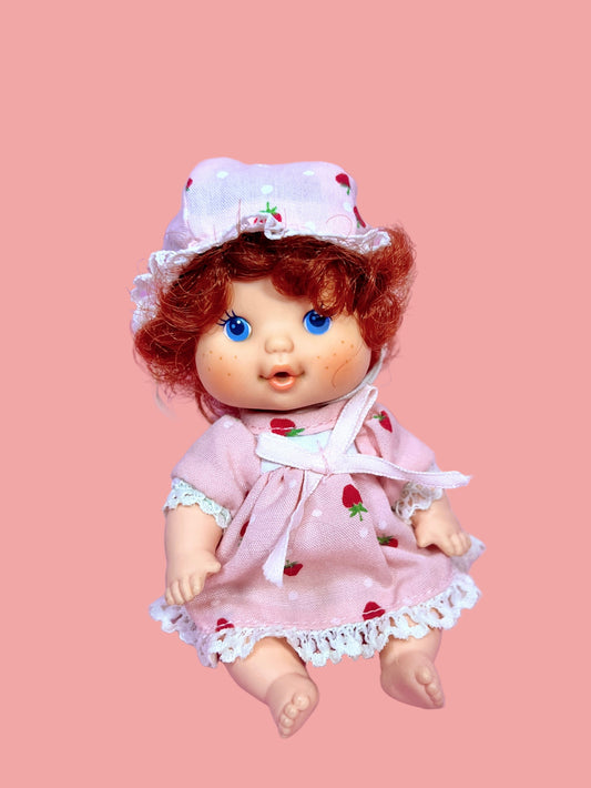 Doll with red hair and a strawberry-themed outfit on a pink background